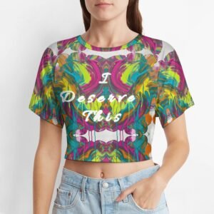 Cropped t‑shirt with vibrant, symmetrical abstract artwork in pink, green, yellow, orange, and blue, featuring the white cursive affirmation ‘I Deserve This’ across the chest. White bands at neckline and hem create a light, balanced frame.
