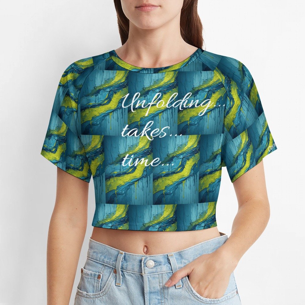 A women’s cropped tee with flowing blue, green, and yellow abstract artwork and the phrase “Unfolding…takes…time…” printed across the front.